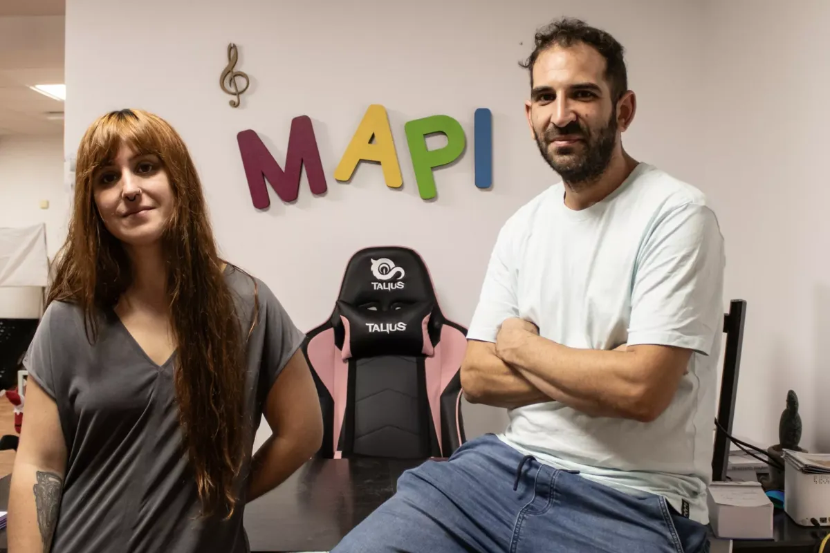 María y Miguel posando juntos con logo de audiovisual Mapi en la pared de fondo.