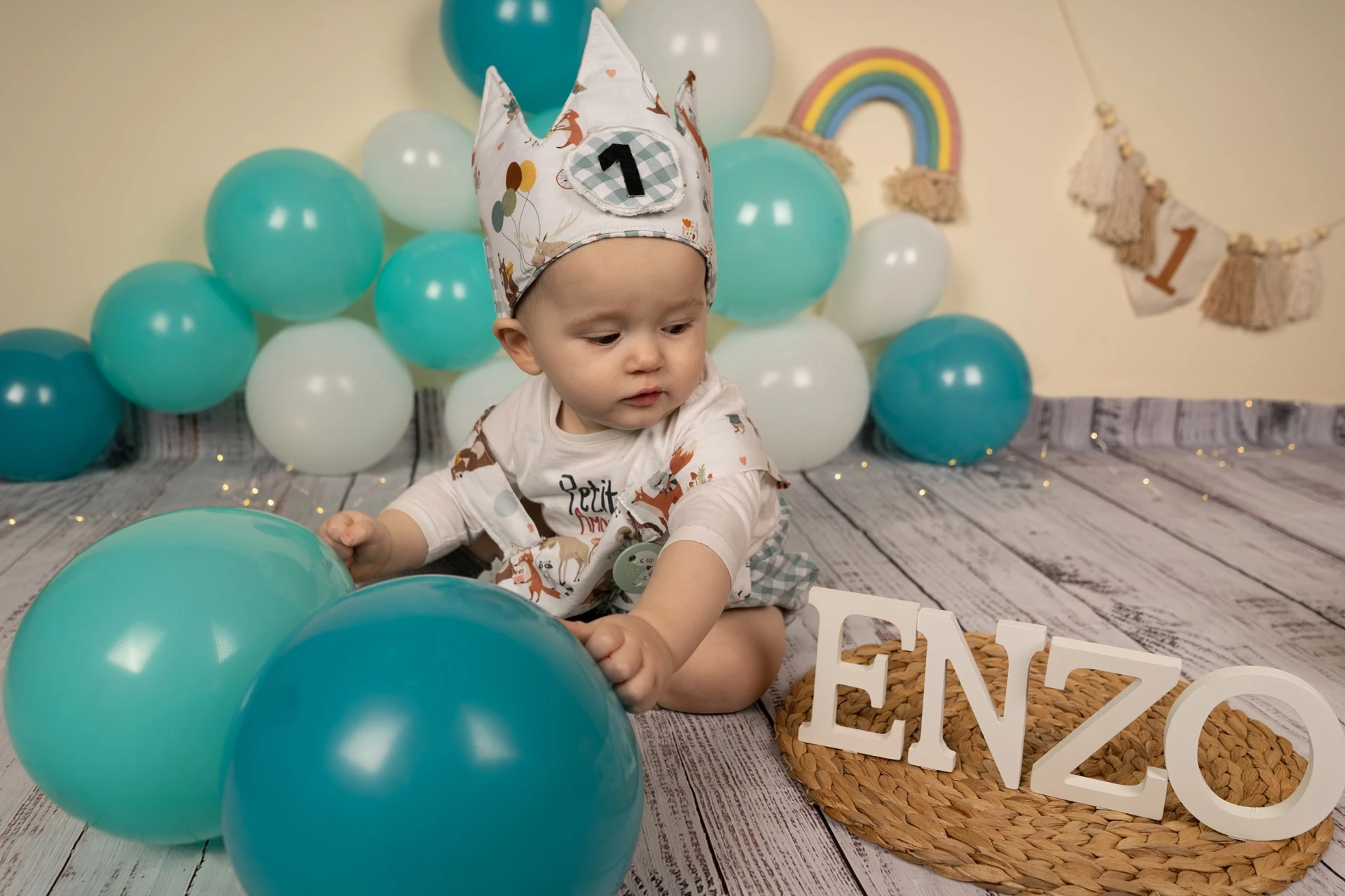 Bebe sentado con globos y su nombre Enzo en letras